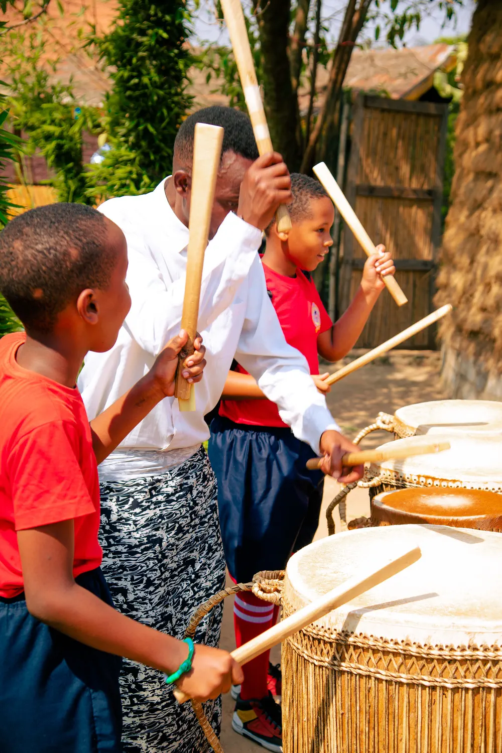 Two boys beating traditional drums with a teacher