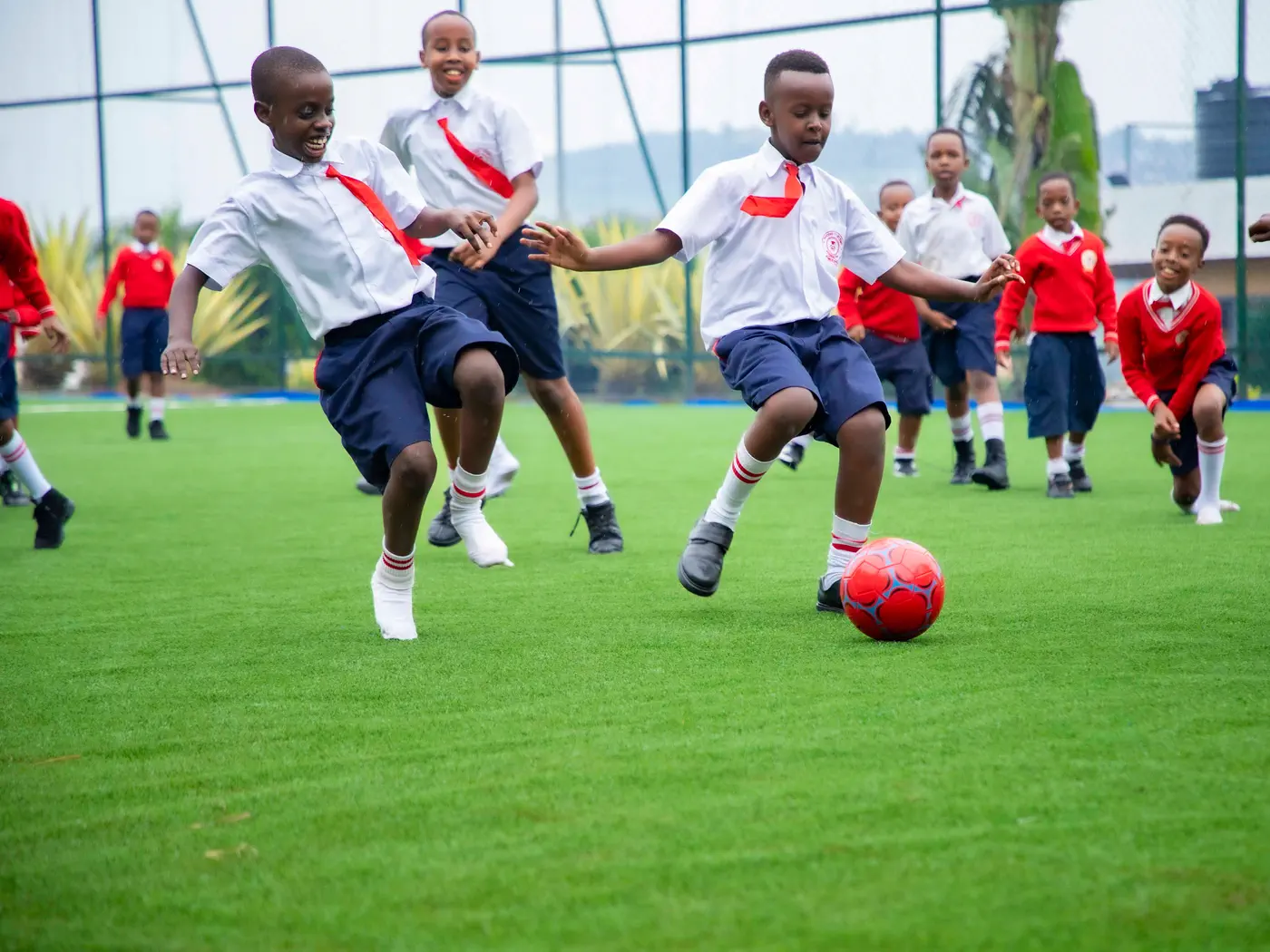 Boys laughing as they chase a football across the pitch