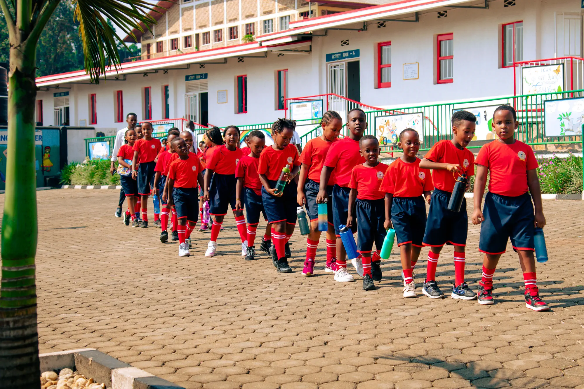 Pupils walking in a line across the school yard, in front of the classroom block