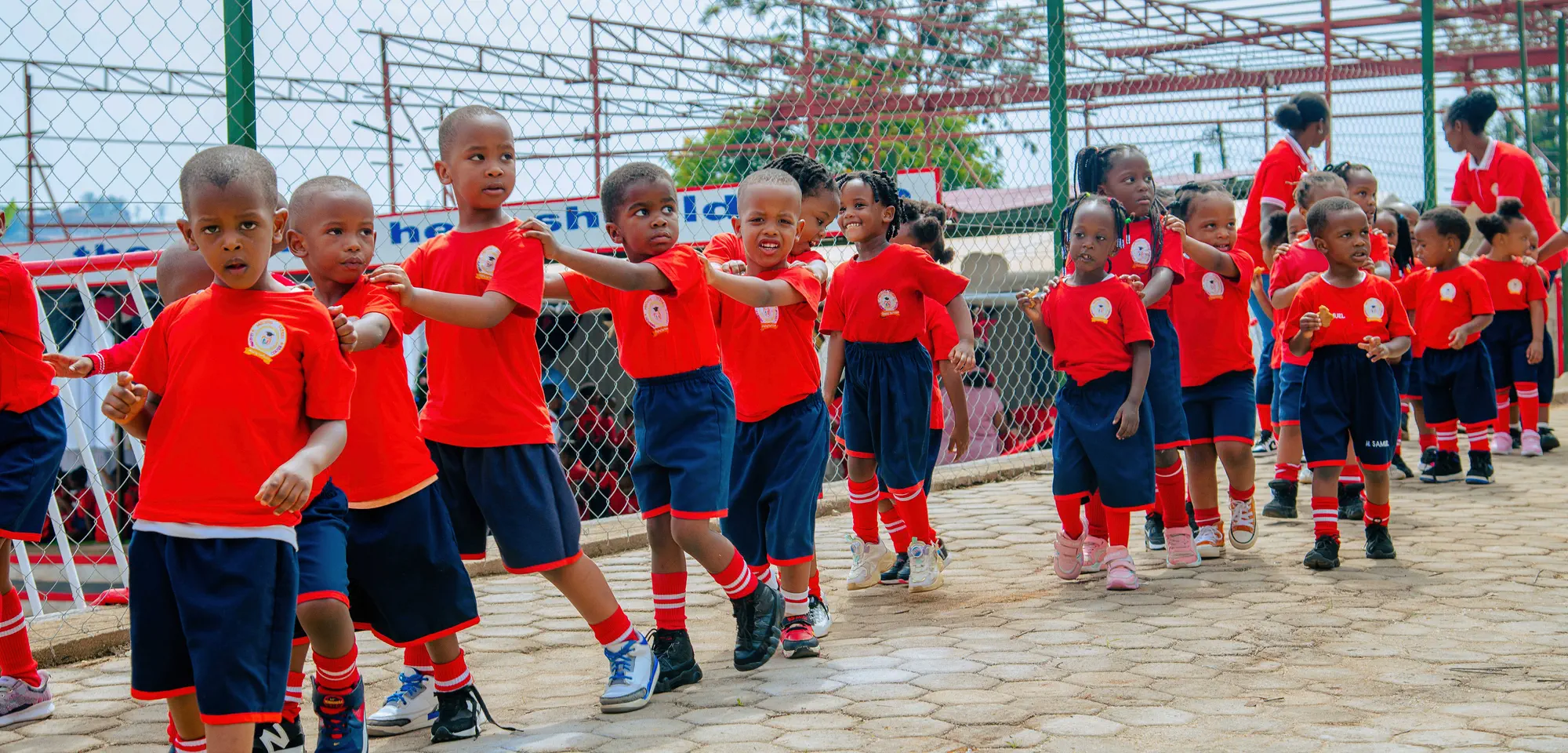 Young pupils in red and navy uniform walking in a line across the school yard