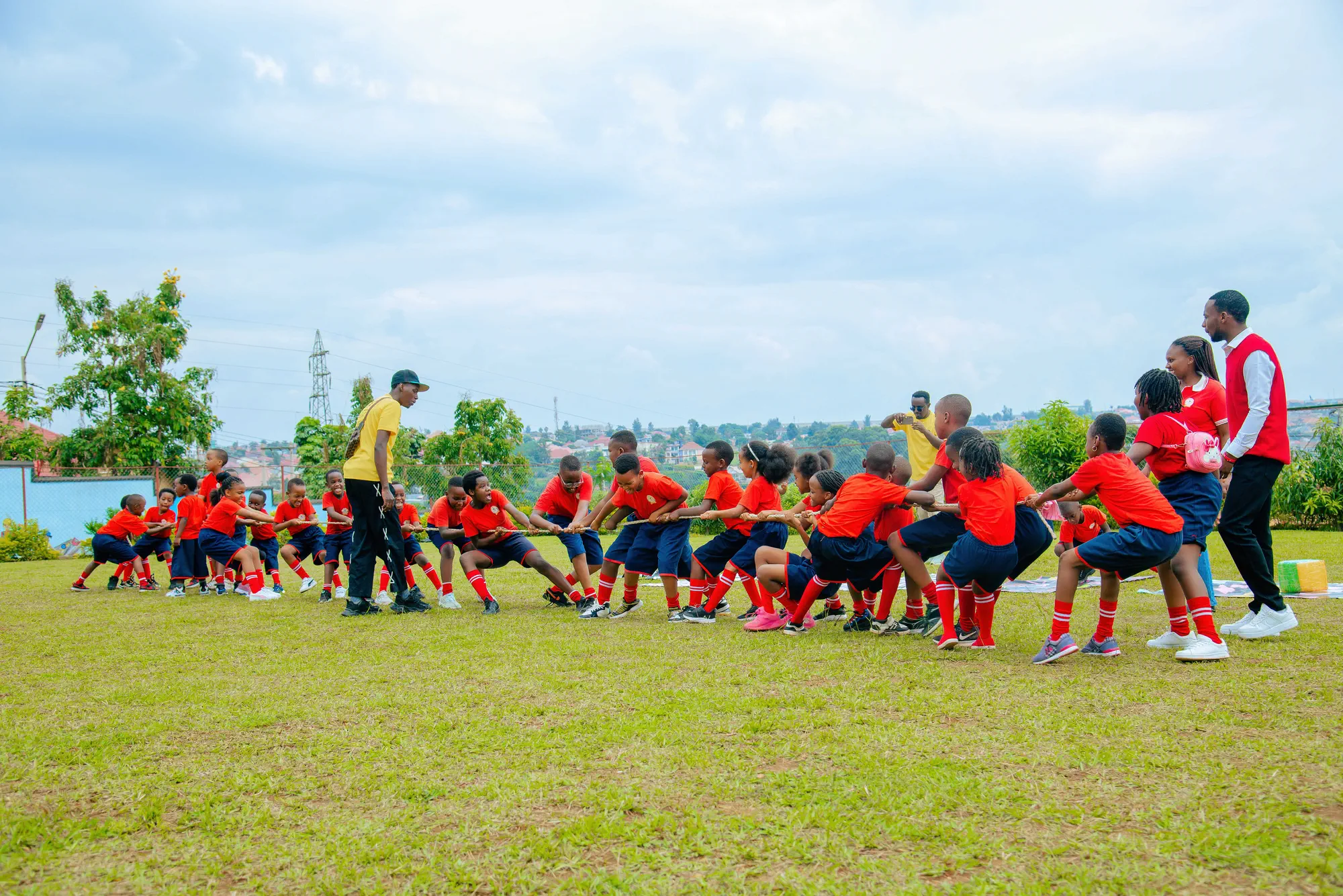 Pupils pulling together in a tug of war on the school field while teachers look on