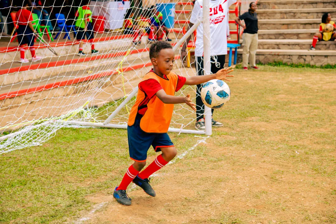 A boy in an orange bib about to throw the football out from his goal on Sports Day