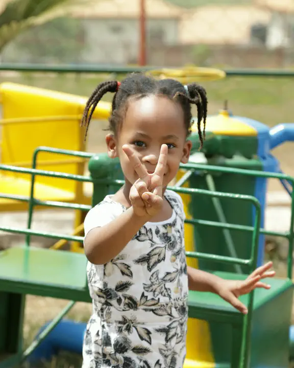 A toddler on the playground making a peace sign