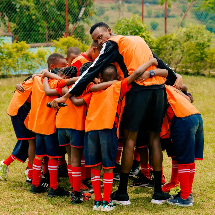 A football team in orange bibs huddled together with their coach